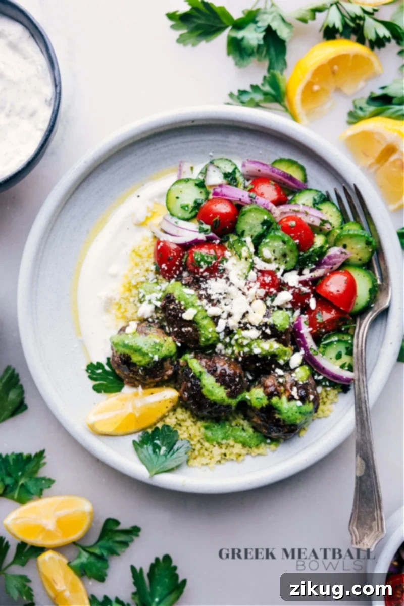 Overhead image of Greek Meatball Bowls, showcasing perfectly cooked meatballs, vibrant salad, fluffy couscous, and a drizzle of lemon-herb sauce