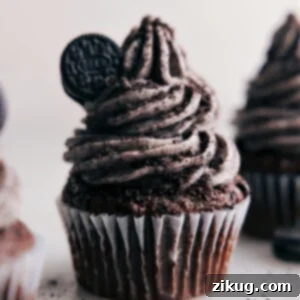 A charming cupcake adorned with a generous swirl of homemade Oreo Frosting and a mini Oreo on top, showcasing its delicious appeal.