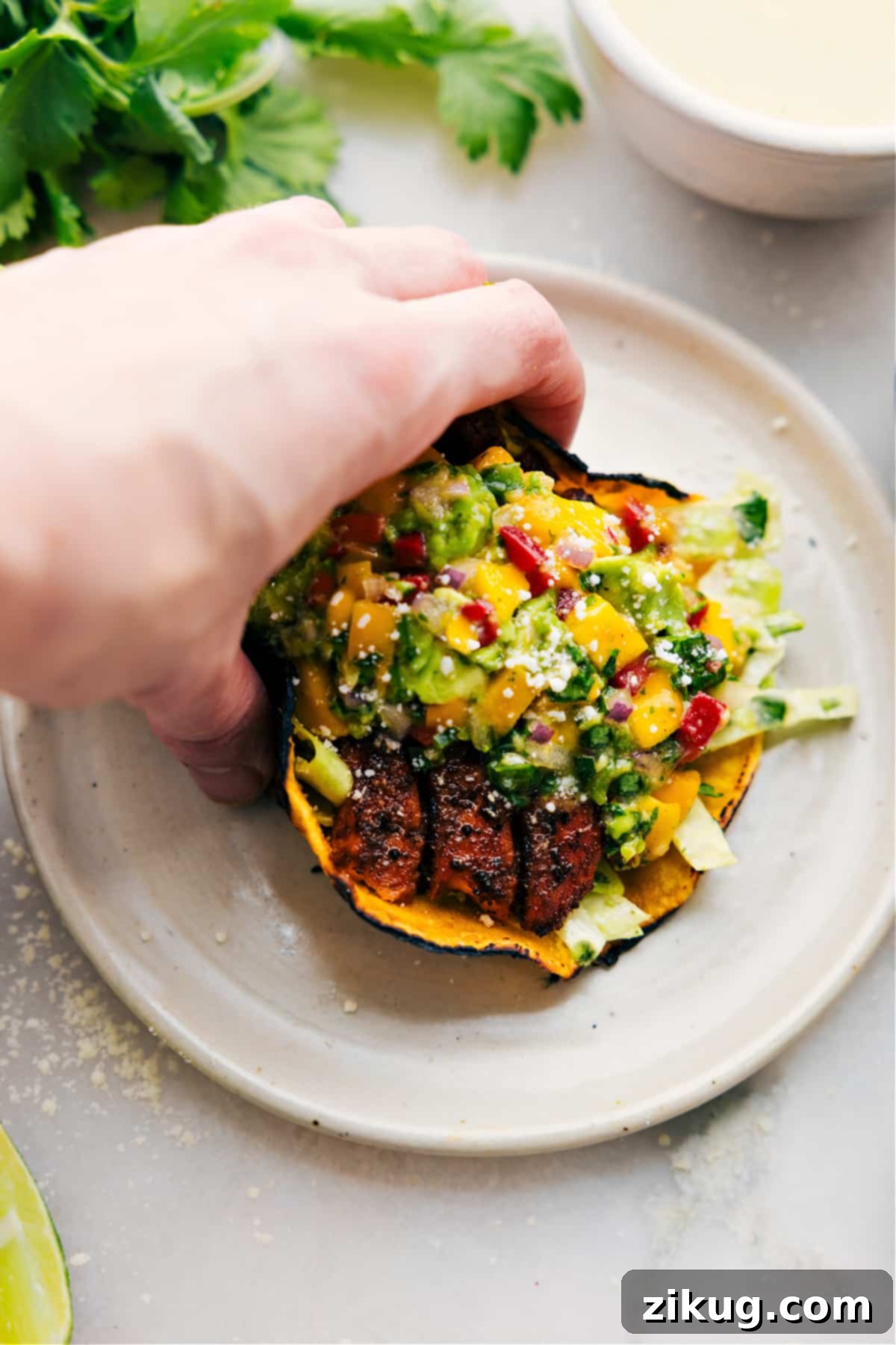 Close-up of three vibrant Salmon Tacos on a plate, garnished with fresh cilantro and a lime wedge.