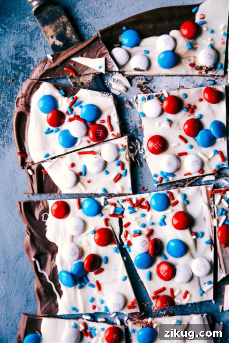 This 4th of July Bark Recipe is the perfect patriotic treat! This dessert is so tasty and with only four ingredients and no baking required, what's not to love?! Recipe via ChelseasMessyApron #festive #chocolate #whitechocolate #m&ms #sprinkles #dessert #treat #fourthofjuly #bark Overhead image of the Fourth of July Bark, featuring red, white, and blue M&Ms and sprinkles on a layered chocolate bark.