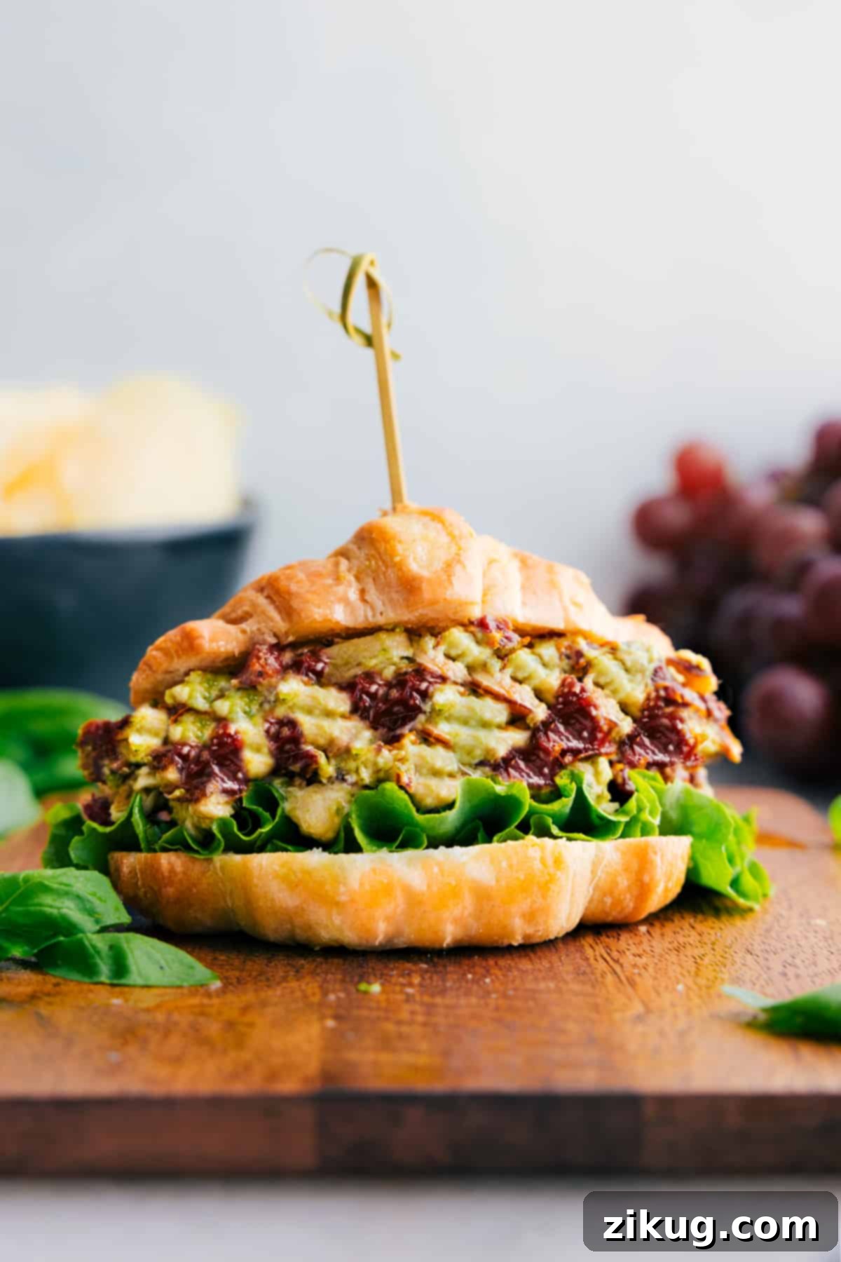 The Best Pesto Chicken Salad Sandwich A delicious Pesto Chicken Salad sandwich alongside fresh grapes and crispy potato chips, perfect for a satisfying lunch.