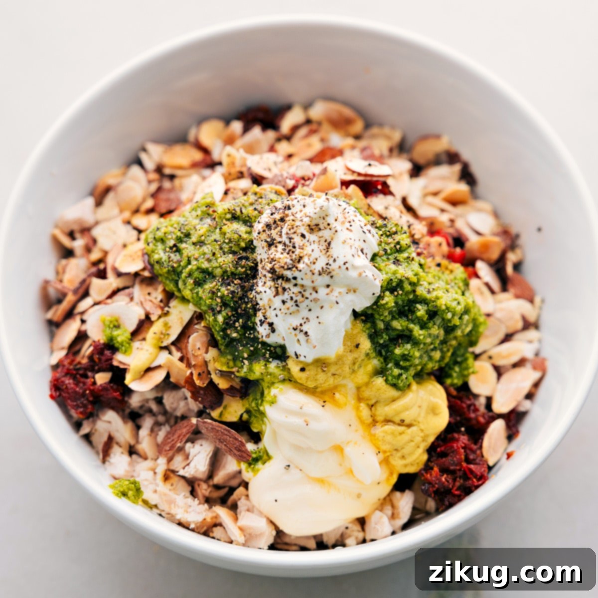 Ingredients Combined for Pesto Chicken Salad All the prepared ingredients, including cubed chicken, diced peppers, sun-dried tomatoes, and almonds, are added to a large bowl, ready for the dressing and a gentle stir.