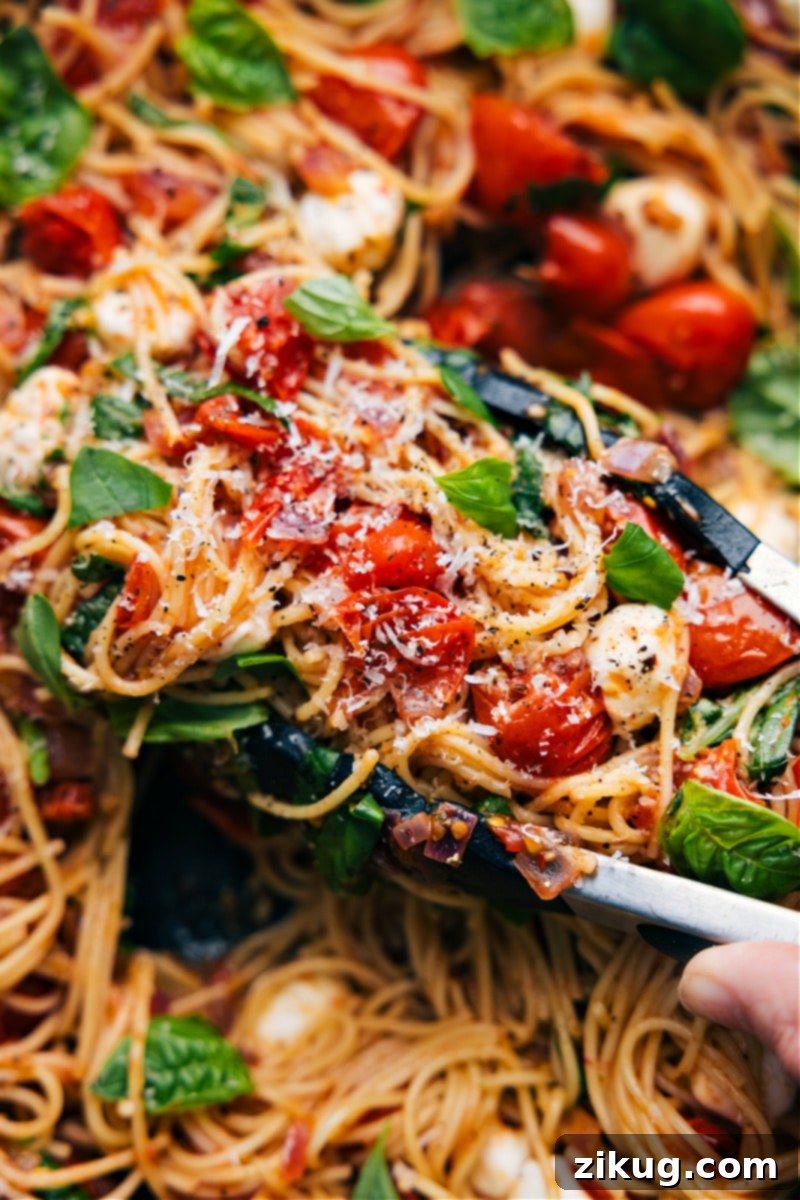 This Caprese Pasta begins with a sauce combining sweet cherry tomatoes, onions, and a hint of garlic. Balsamic vinegar and honey add a tangy-sweet kick while angel hair pasta, fresh basil, and creamy mozzarella finish off this comforting and delicious Italian-inspired dish. Recipe via chelseasmessyapron #dinner #quick #easy #simple #familyfriendly #kidfriendly #comfortfood #tomatoes #basil #pesto #caprese #pasta Overhead image of Caprese Pasta, a vibrant dish featuring pasta, halved cherry tomatoes, fresh basil, and mozzarella pearls in a light sauce.