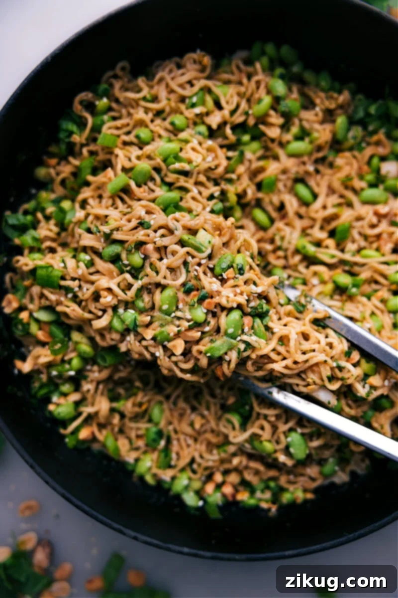 Overhead image of a bowl of Peanut Butter Ramen, garnished with green onions, sesame seeds, and chopped peanuts.