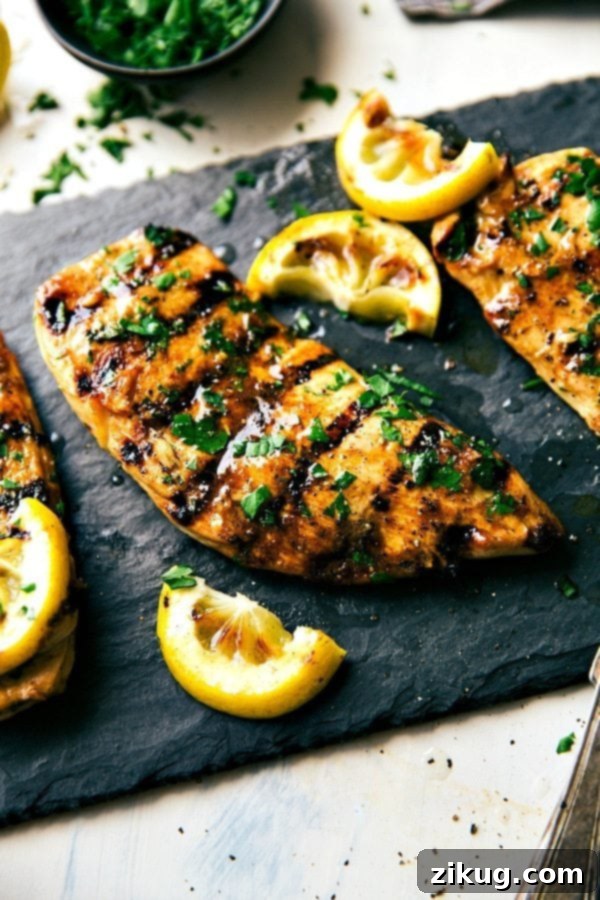 The best grilled chicken marinade, garnished with fresh herbs on top and lemon juice ready to be cut up and enjoyed for added flavor.