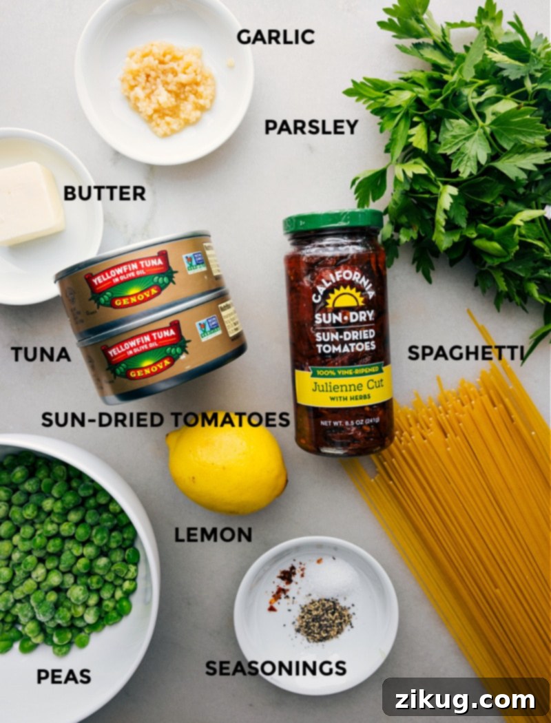 Ingredients for Healthy Tuna Pasta Recipe A vibrant display of fresh and pantry ingredients laid out on a wooden surface, including uncooked spaghetti, bright green peas, oil-packed sun-dried tomatoes, a fresh lemon, and a can of tuna, all ready for the Healthy Tuna Pasta recipe preparation.