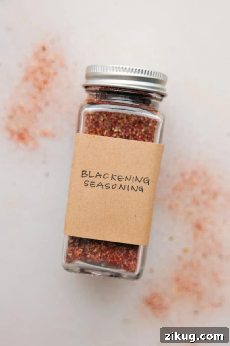 This Blackening Seasoning recipe creates a versatile, smoky, and spicy blend perfect for forming a flavorful crust on grilled or pan-fried dishes. Easily homemade, it combines everyday spices and can be stored for future use, bringing a robust flavor to meats, fish, and vegetables. A charming glass jar filled with vibrant homemade blackened seasoning, prominently displayed against a rustic kitchen backdrop, ready to infuse meals with robust flavor.