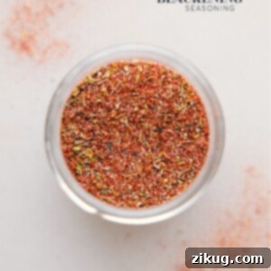 A close-up image of homemade Blackened Seasoning in a small ceramic bowl, with a wooden spoon resting nearby, highlighting its rich color and texture.