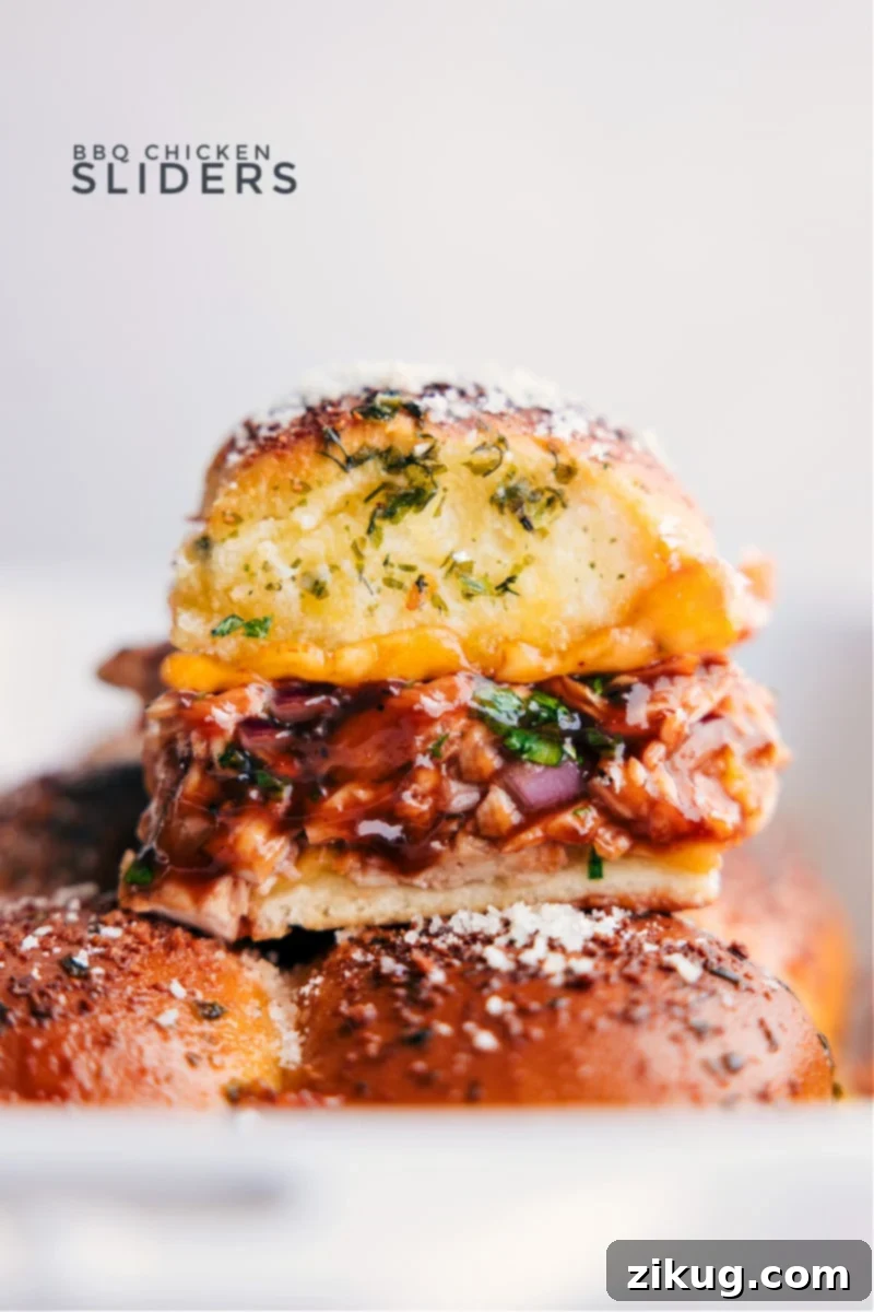 These BBQ Chicken Sliders combine juicy BBQ chicken, melty Gouda cheese, and sweet Hawaiian rolls, all jazzed up with a pop of onion and cilantro. The rolls are brushed with garlic-herb butter that gives these sliders a beautiful crispy and golden exterior. Recipe via ChelseasMessyApron.com #BBQ #BBQchicken #sliders #hawaiianrolls #quick #easy Close-up view of golden-brown BBQ Chicken Sliders with a vibrant filling