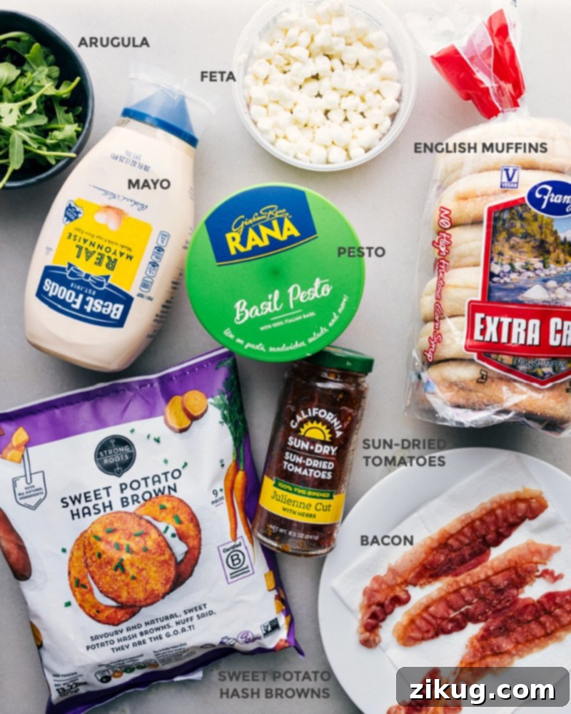 Essential Ingredients for Your Delicious English Muffin Sandwich A selection of fresh ingredients laid out, including vibrant arugula, crumbled feta cheese, creamy mayonnaise, fragrant basil pesto, juicy sun-dried tomatoes, toasted English muffin halves, crispy sweet potato hash browns, and perfectly cooked bacon strips.