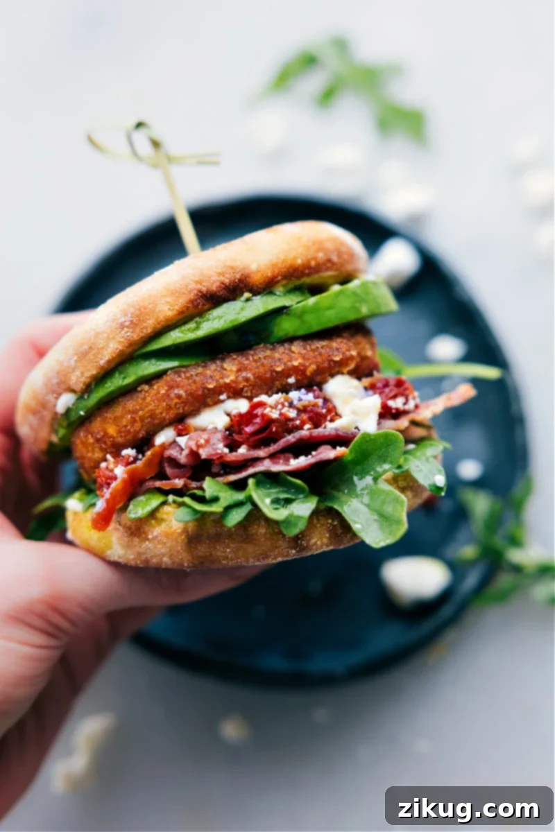Simple Yet Incredibly Delicious English Muffin Sandwich Recipe A close-up of a perfectly constructed English Muffin Sandwich being held, showcasing the rich layers of ingredients including crispy bacon, creamy avocado, pesto, feta, and a golden sweet potato hash brown within the toasted muffin.