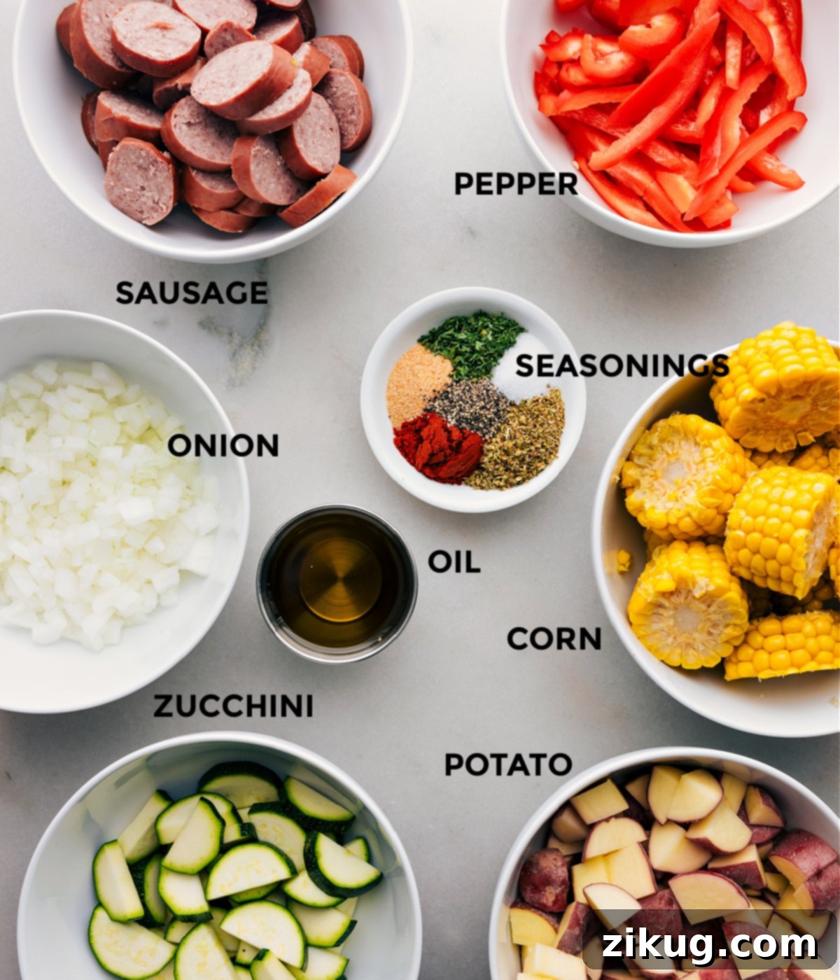 Key Ingredients In Our Delicious Tin Foil Sausage and Veggies Dinner All the fresh ingredients including smoked sausage, colorful bell peppers, onion, potatoes, corn, zucchini, olive oil, and seasonings laid out and prepped for assembly into tin foil packets.