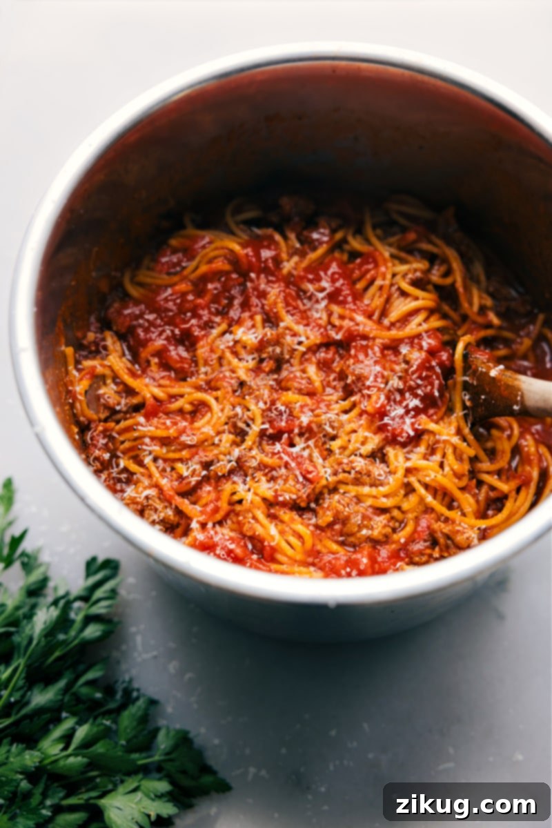Family-friendly Instant Pot Spaghetti, ready to enjoy. Overhead view of a full Instant Pot filled with cooked spaghetti and rich sauce, garnished with fresh herbs, ready for serving.