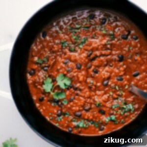 A bowl of rich Pumpkin Chili with a wooden spoon