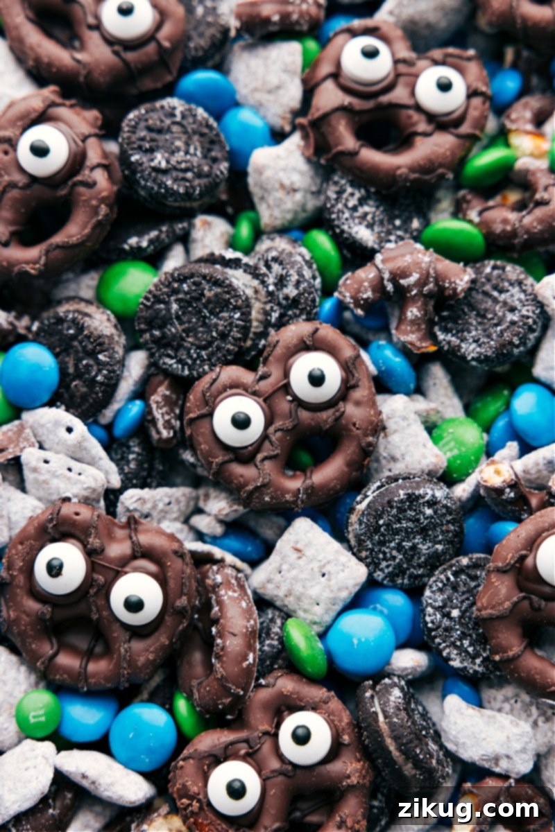 These Goblin Goodies (Halloween Muddy Buddies) are a fun Halloween treat, bursting with rich flavors of chocolate and peanut butter, complemented by the crunch of cereal, Oreos, and M&M's. It's a spooky and delicious snack mix you won't want to miss! Recipes via ChelseasMessyApron.com #halloween #oreos #M&Ms #chex #muddybuddies #snackmix. Closeup view of Goblin Goodies showing a variety of textures including powdered sugar-dusted cereal, mini Oreos, colorful M&M's, and the whimsical edible eye pretzels.