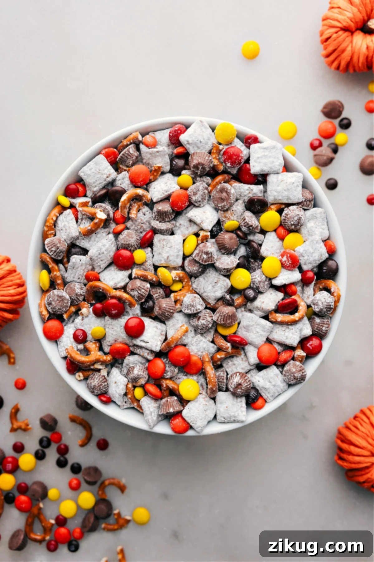 Autumnal Delight: A Bowl of Festive Fall Muddy Buddies Ready to Enjoy! A bowl of Fall Muddy Buddies, showcasing the delightful mix of cereals coated in chocolate and powdered sugar, punctuated by autumn-themed candies and snacks for a festive treat.