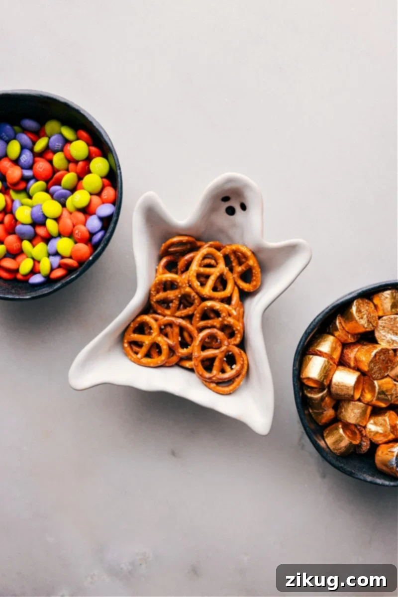 The simple yet essential ingredients for Monster Eyeballs: M&M's for color, pretzels for crunch, and Rolos for the melty caramel core. A close-up image showing the three main ingredients required for Monster Eyeballs: a bag of M&M's, a bag of pretzel twists, and a roll of Rolo caramel chocolates.