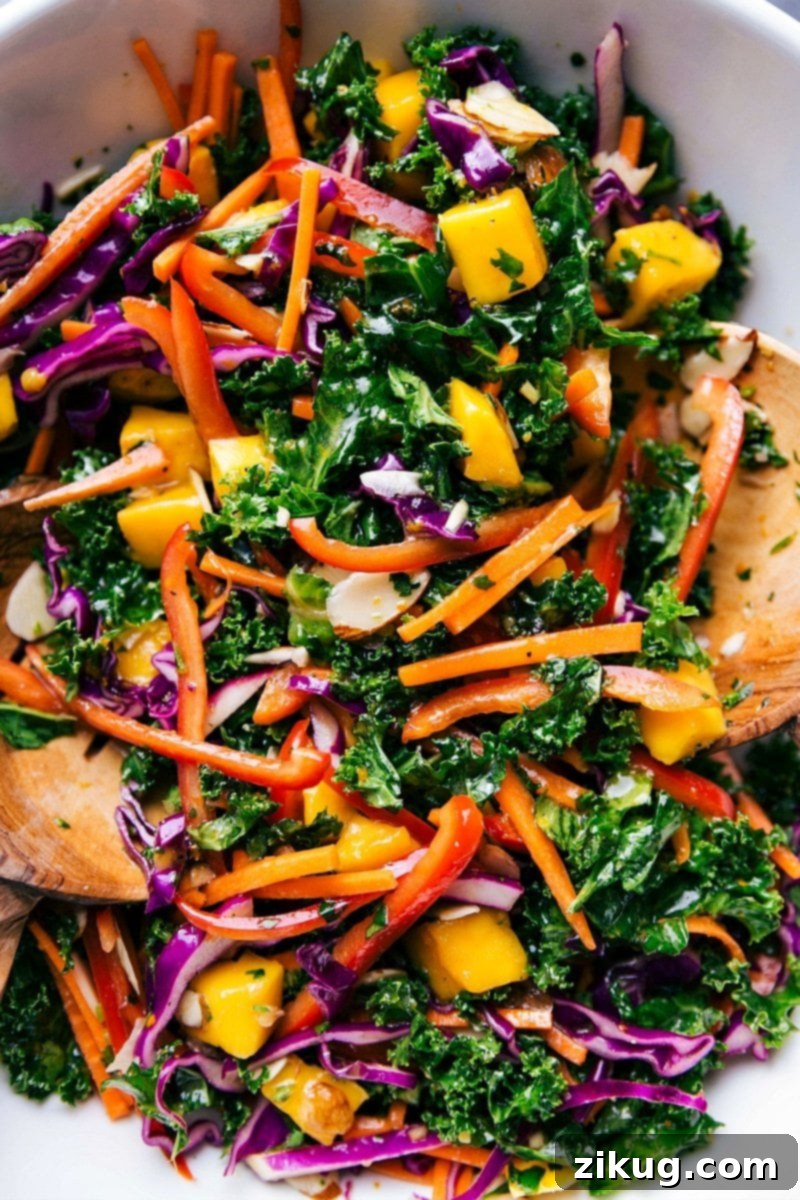 Healthy and vibrant kale salad served in a bowl, accompanied by wooden serving spoons. Colorful bowl of the completed kale salad recipe, complete with wooden serving spoons.
