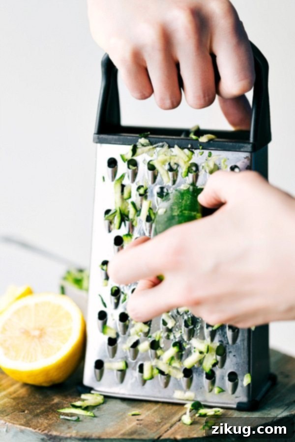 Shredding fresh zucchini on a box grater, a vital step in preparing the lemon zucchini bread recipe.