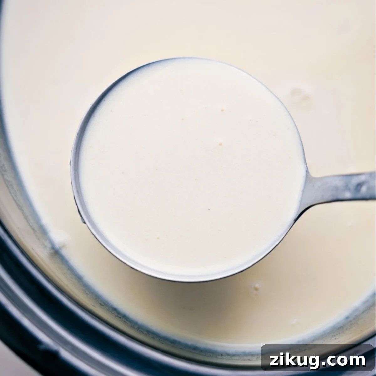 A ladle full of the warm and freshly prepared White Hot Chocolate, smooth and inviting, ready to be served into mugs. Steam rises gently from the rich beverage.