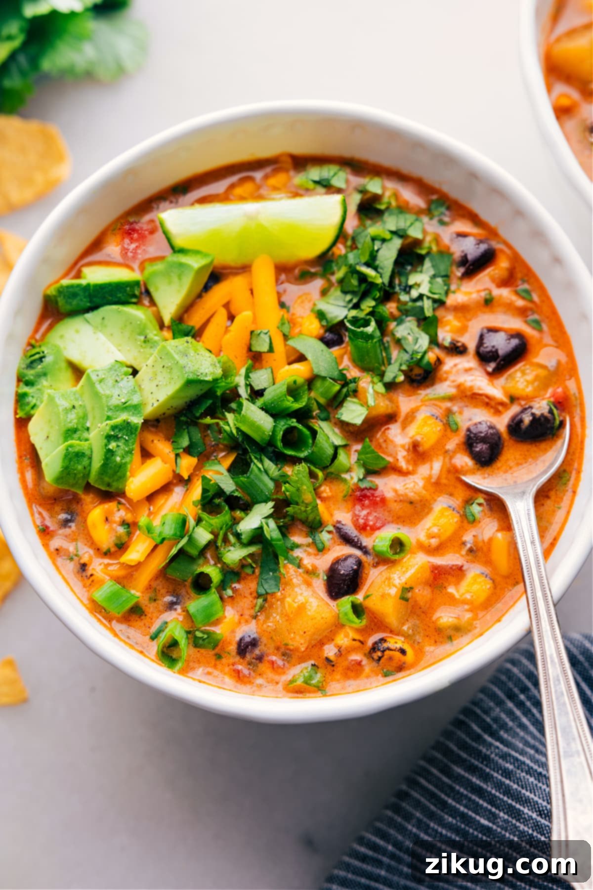 A bowl of the southwestern corn chowder with black beans, generously topped with green onions, melted cheese, and sliced avocados, ready to be enjoyed.