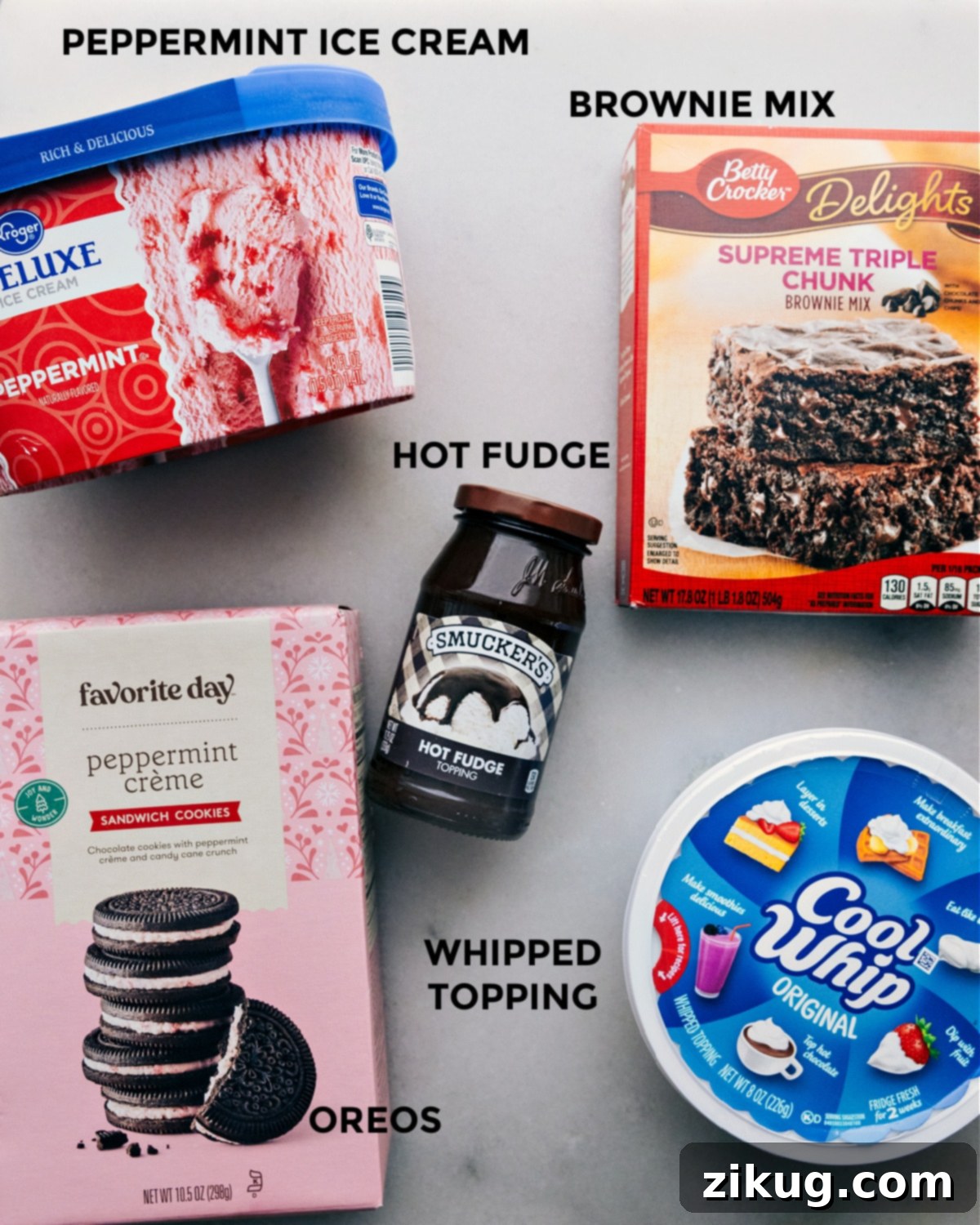Five Ingredients for Peppermint Brownie Ice Cream Bars A flat lay photograph displaying the five essential ingredients laid out on a clean surface, including a box of brownie mix, a package of Oreo cookies, a jar of hot fudge topping, a tub of peppermint ice cream, and a container of whipped topping, clearly illustrating the simplicity of the recipe.