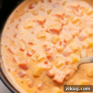 A close-up of a rustic bowl of Cheesy Potato Soup, garnished with crispy bacon, chopped chives, and a dollop of sour cream, reflecting its rich and comforting nature.