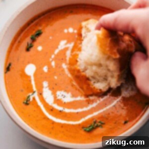 Big bowl of Roasted Red Pepper Soup being dipped with bread.