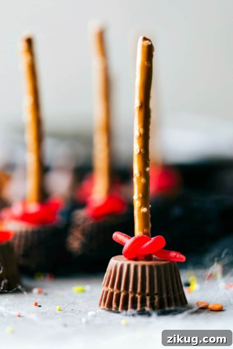 Image of a witch's broom, standing upright against a dark background, showcasing its pretzel stick handle and Reese's cup base with licorice bristles.