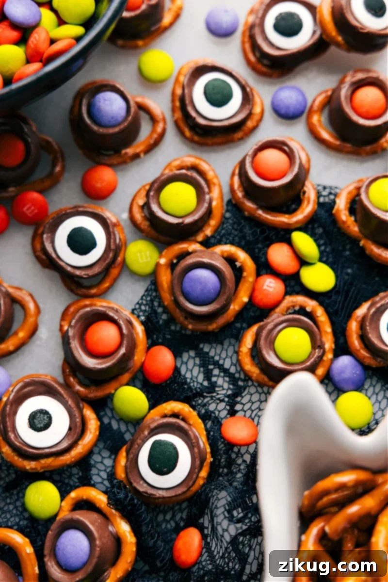 An overhead view of Monster Eyeballs, featuring pretzel twists, melted Rolos, M&Ms, and large candy eyeballs, arranged on a dark surface.
