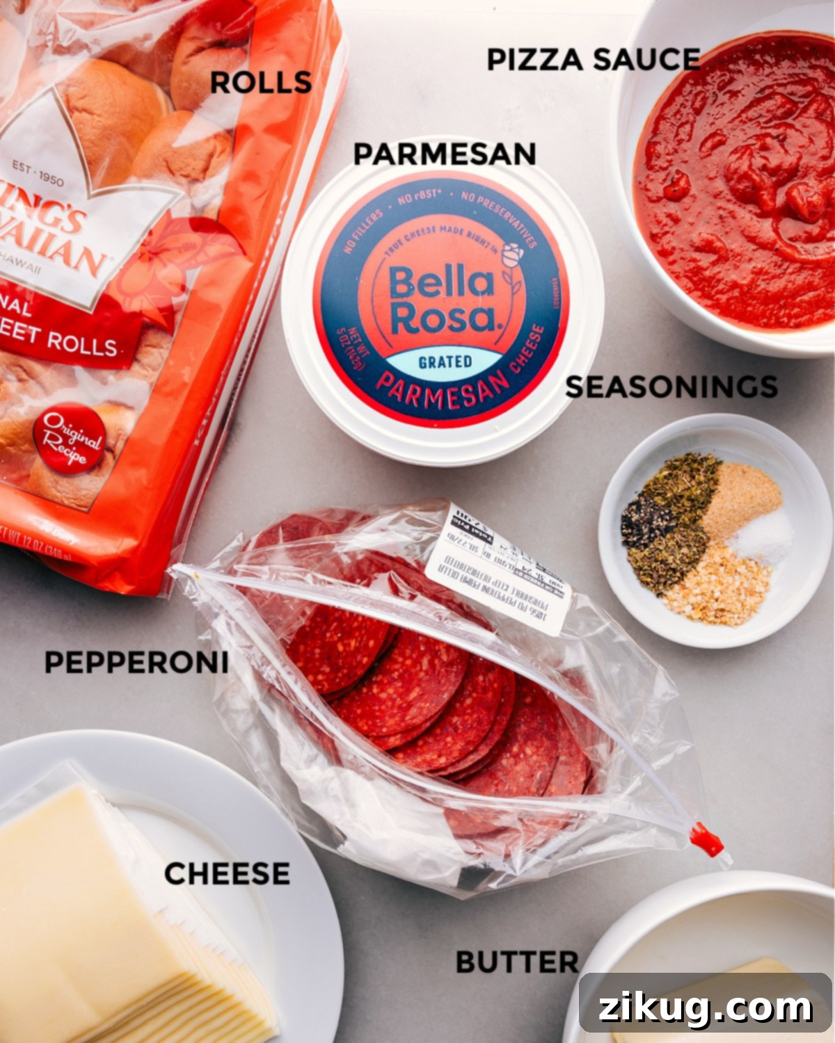 A vibrant display of all fresh ingredients for Pizza Sliders laid out on a counter, including Hawaiian rolls, mozzarella, pepperoni, pizza sauce, butter, and various seasonings.