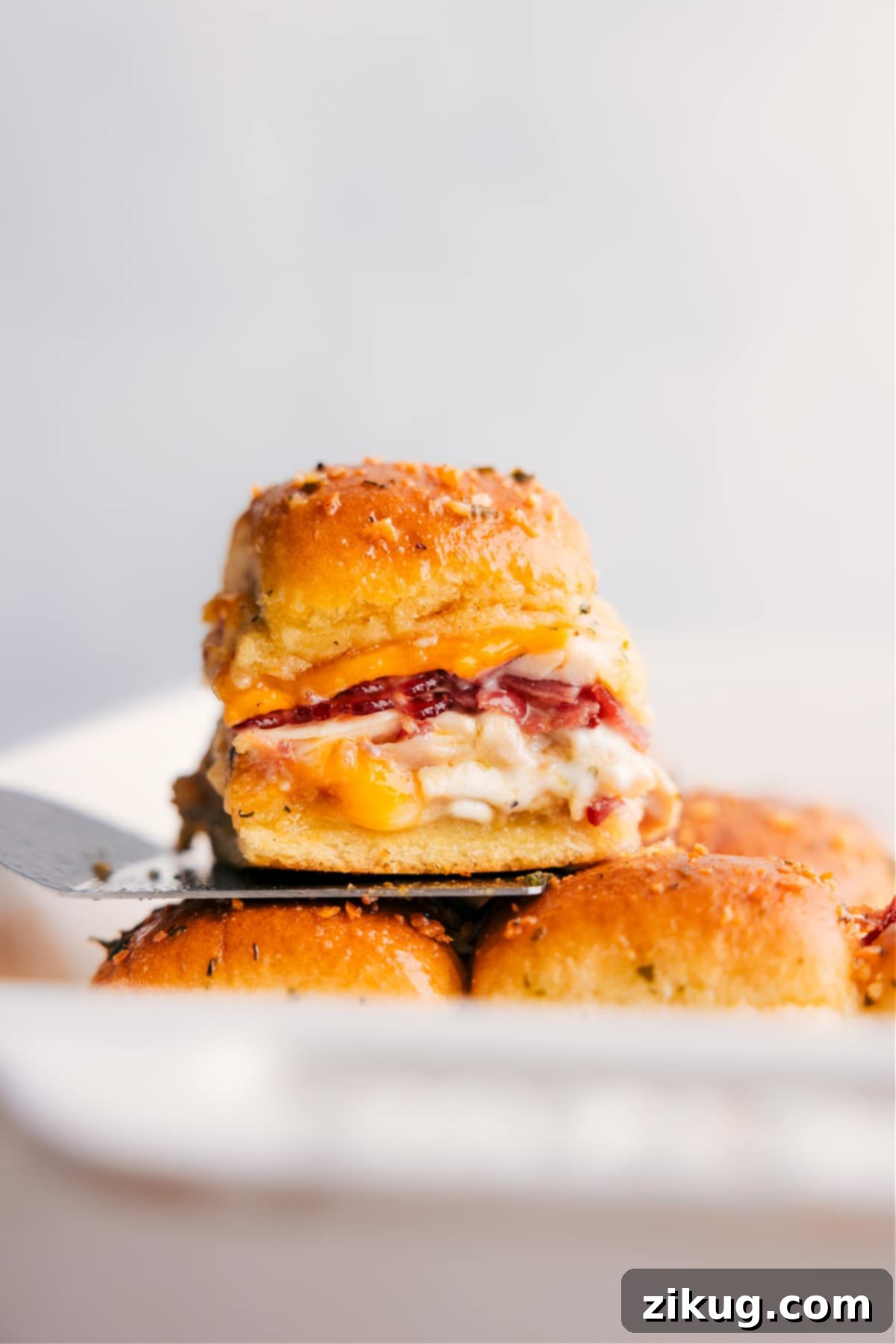 Mouthwatering Chicken Bacon Ranch Sliders – the perfect party food or quick meal! A stack of golden brown Chicken Bacon Ranch Sliders, with one perfectly melted slider on a spatula, ready to be served.