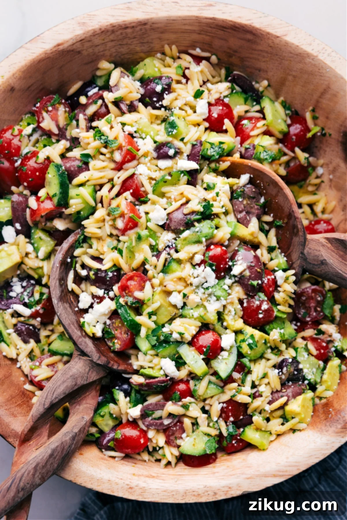 Mediterranean Orzo Salad - A Perfect Summer Dish Wooden spoons, tossing a batch of Mediterranean Orzo Salad.