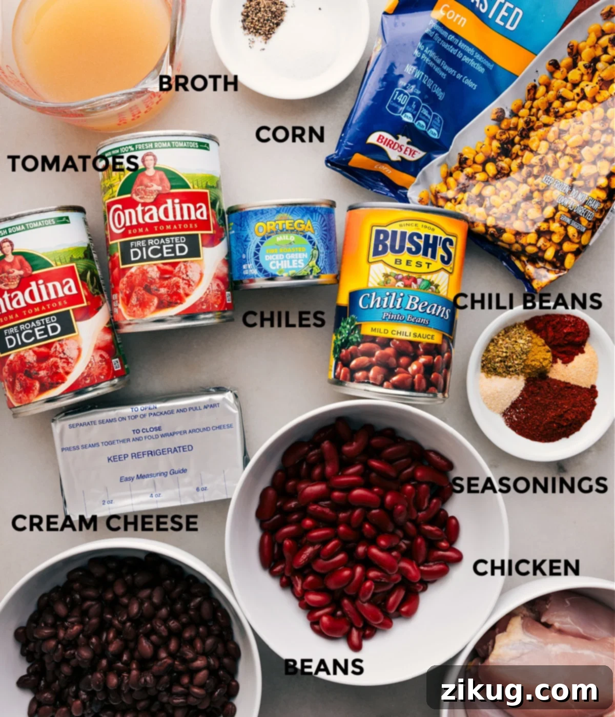 A beautiful flat lay of fresh and canned ingredients like chicken broth, various seasonings, corn, an assortment of beans, fire-roasted tomatoes, green chiles, and a block of cream cheese, all prepped for an effortless slow cooker chili.