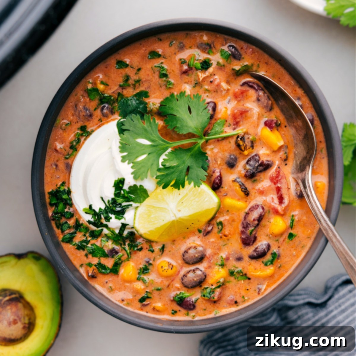 A hearty bowl of creamy chicken taco chili, generously topped with shredded cheese, fresh avocado, a dollop of sour cream, and a sprinkle of cilantro, ready to be enjoyed.