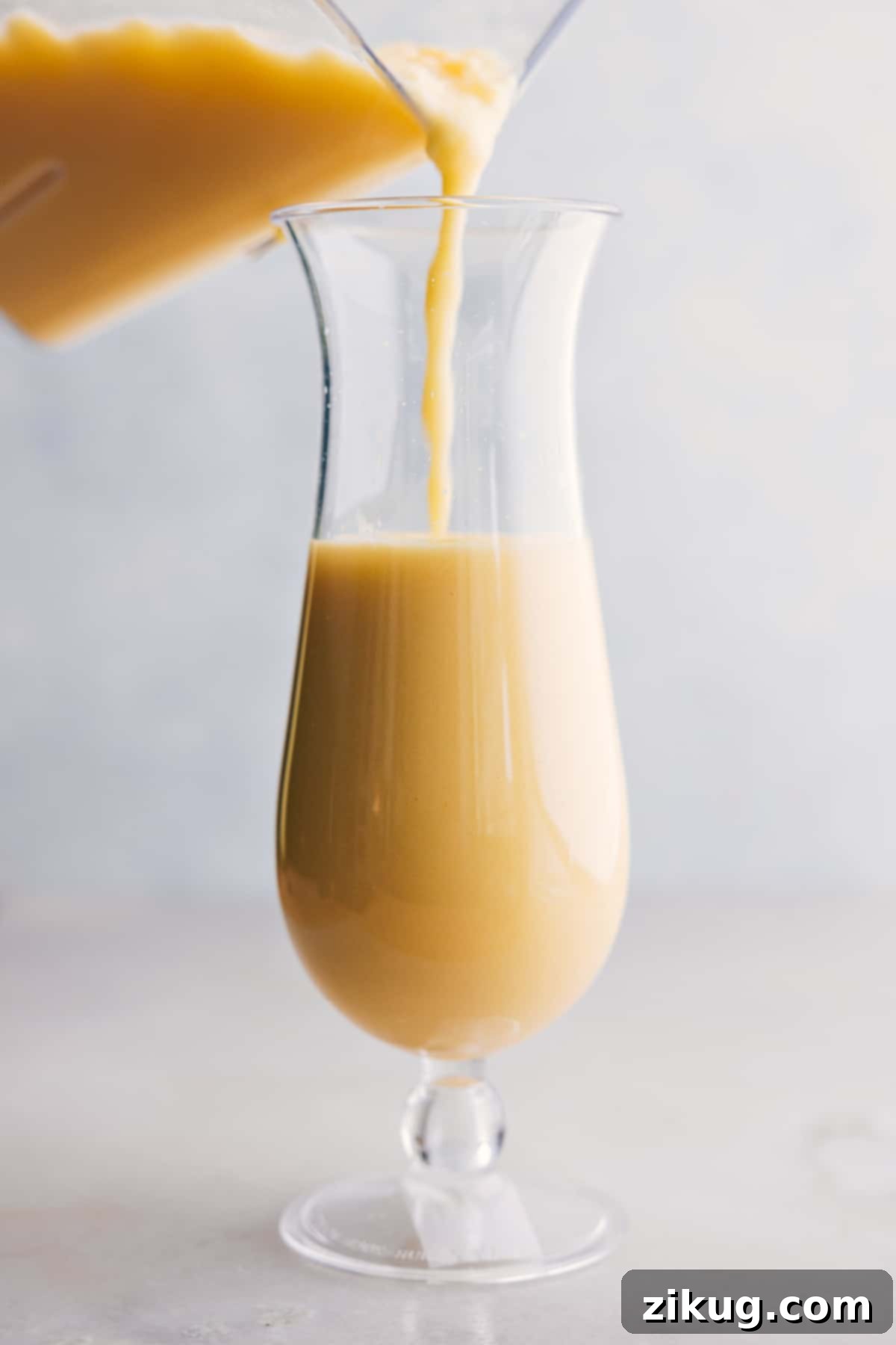 A stream of perfectly blended Pina Colada being poured from a blender into a frosted glass, showcasing its creamy texture.