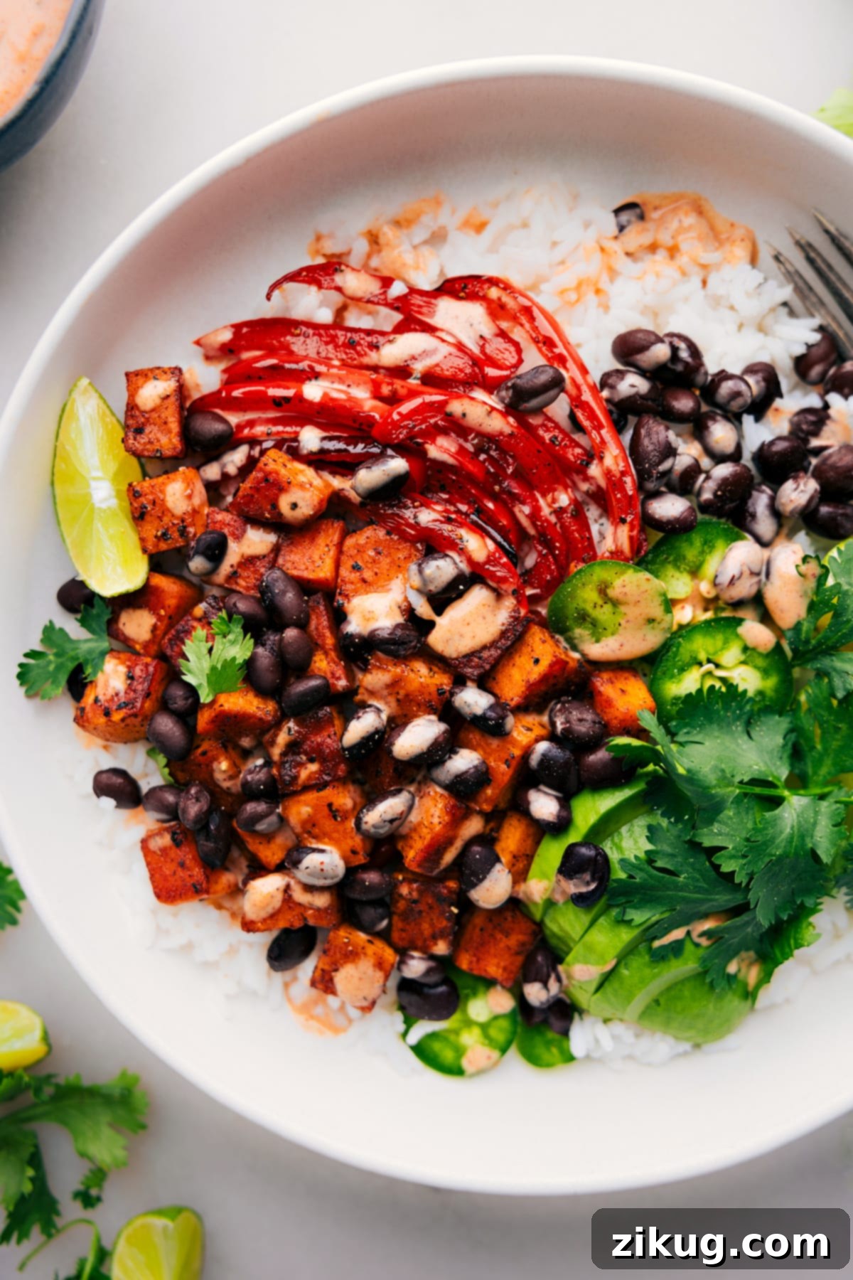 Ready-to-savor Sweet Potato and Black Bean Burrito Bowls: A Feast for the Senses A vibrant and fully assembled Sweet Potato and Black Bean Burrito Bowl, showcasing layers of rice, roasted vegetables, black beans, avocado, and fresh cilantro, all artfully arranged and ready for immediate enjoyment.
