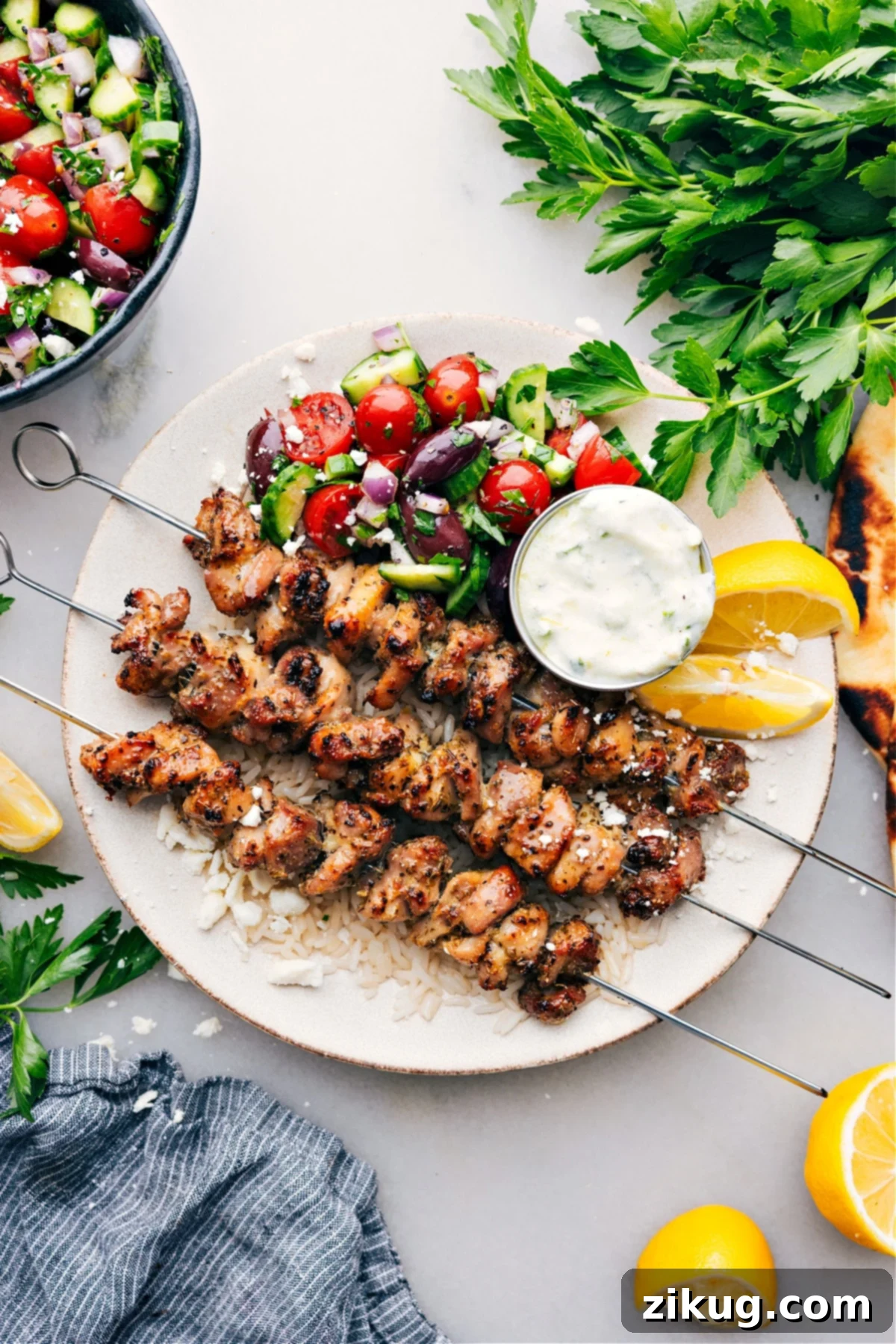 Easy and Healthy Greek Chicken Bowls for Meal Prep A beautifully arranged Greek Chicken Bowl on a white plate, featuring perfectly cooked chicken over rice, alongside a fresh Greek salad, and a dollop of creamy Tzatziki sauce.
