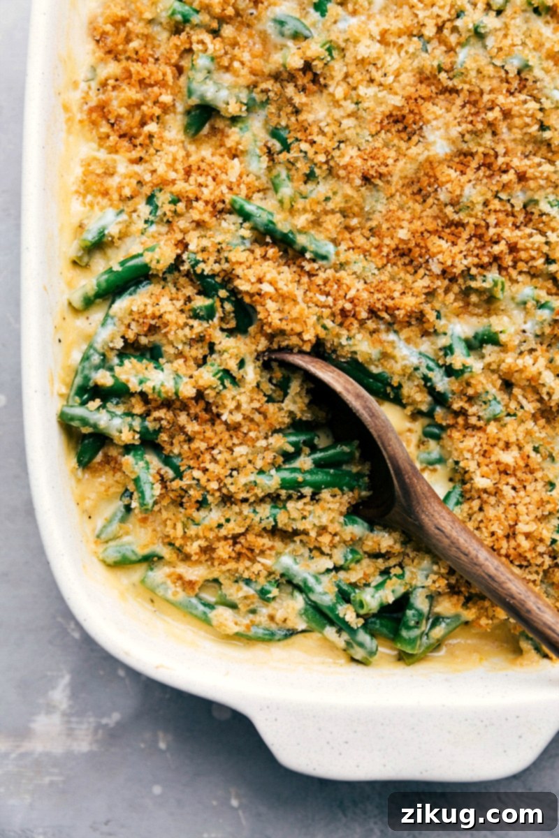 Ready-to-eat homemade green bean casserole in a rustic baking dish, showcasing its golden-brown, crisp panko topping and creamy interior, garnished with fresh herbs and a serving spoon.