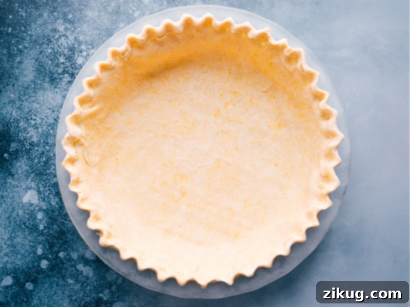 The Best Homemade Pie Crust Ready for Filling A perfectly prepared pie crust nestled in a clear glass pie dish, ready for its delicious pumpkin filling.