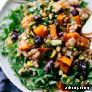 A vibrant Sweet Potato Farro Salad in a white bowl, garnished with fresh herbs, showcasing roasted sweet potatoes, cranberries, and pistachios.