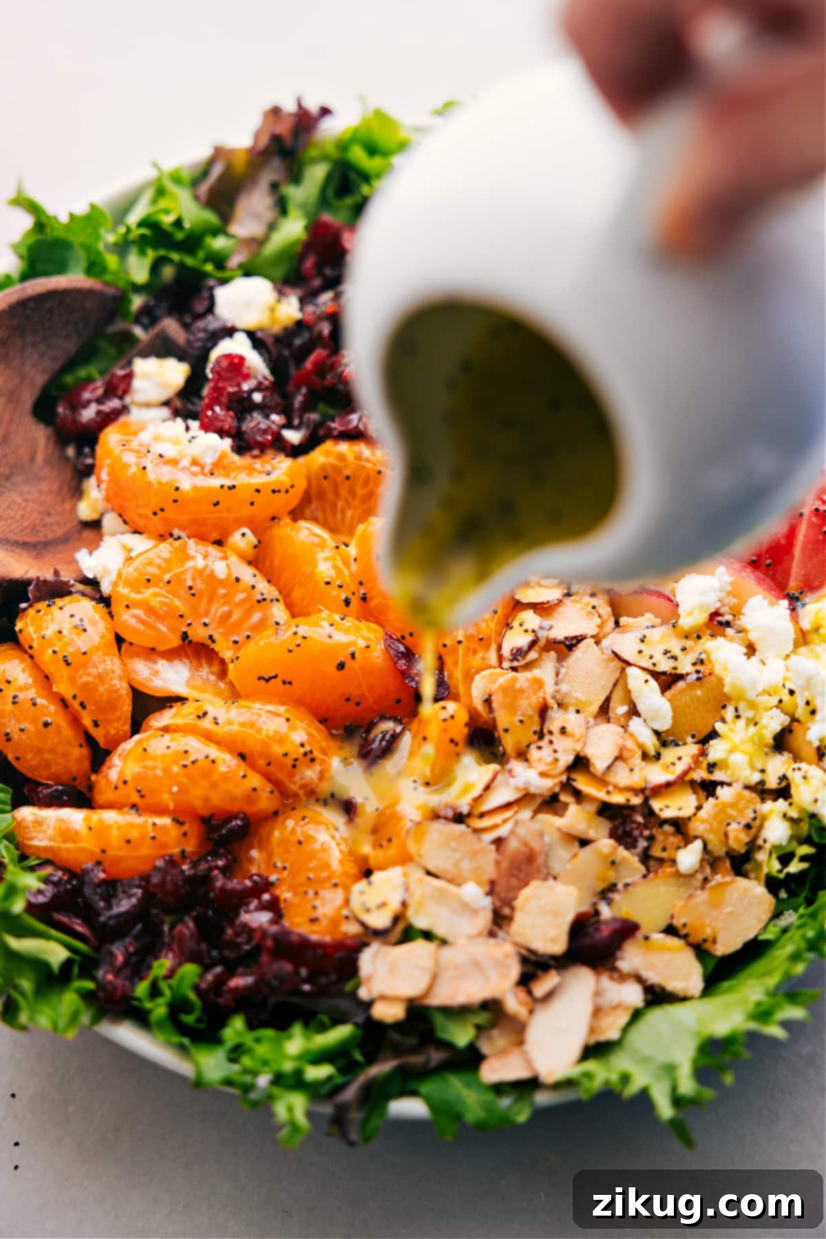 A generous pour of the zesty citrus dressing cascading over the vibrant mandarin orange salad, ready for a gentle toss to combine flavors.