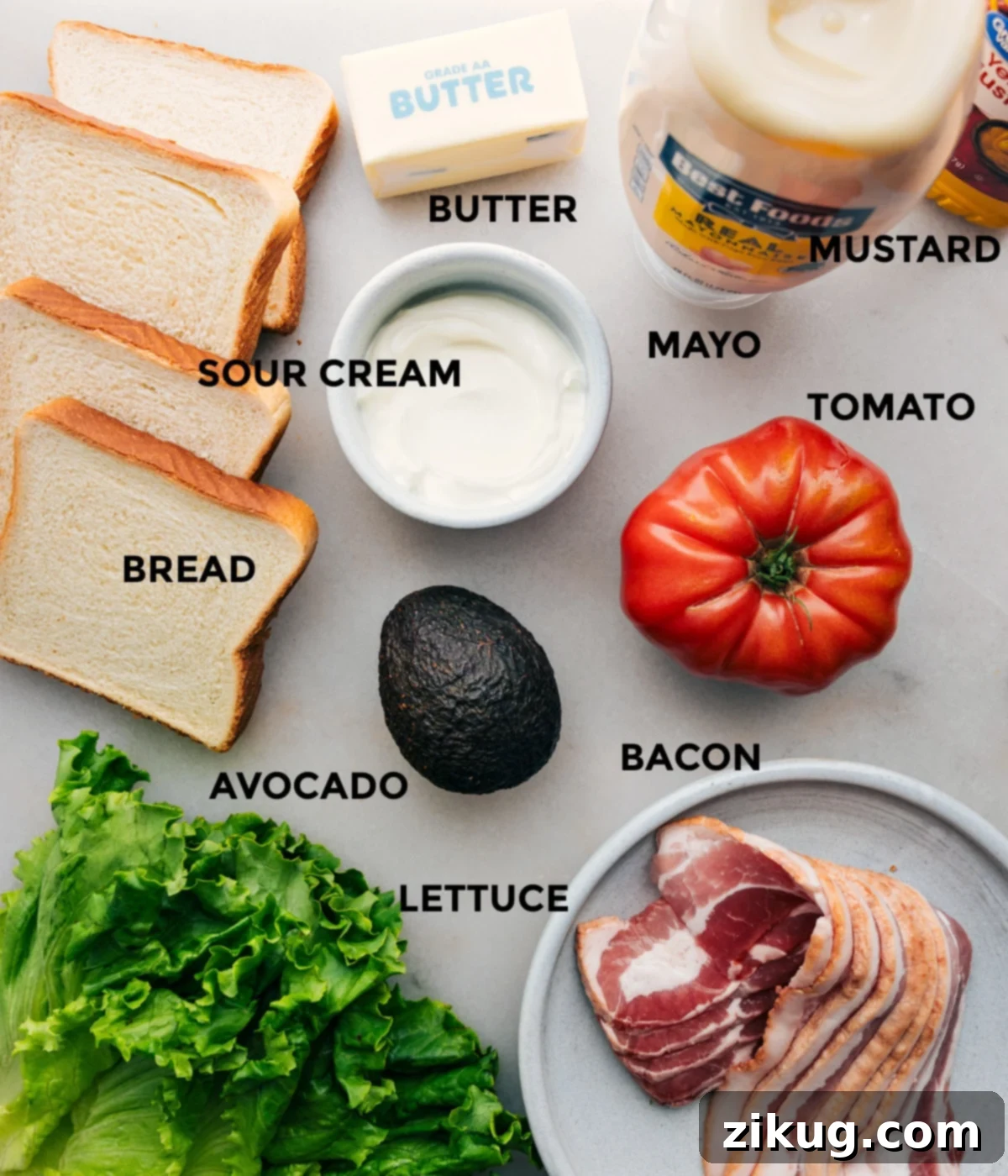 All the ingredients for the perfect BLT sandwich including bread, sour cream, butter, mustard, mayo, tomato, bacon, avocado, and lettuce prepped out for easy assembly.
