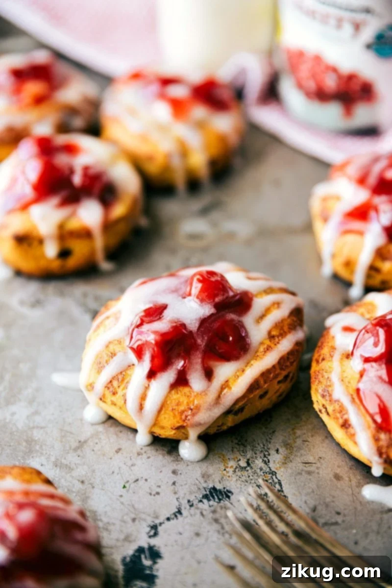 A view of freshly baked Cherry Danish Cinnamon Rolls cooling on a baking sheet, showcasing their golden-brown edges and luscious toppings.