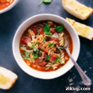 A close-up of a rustic bowl of Chicken Parmesan Soup, garnished with fresh basil.