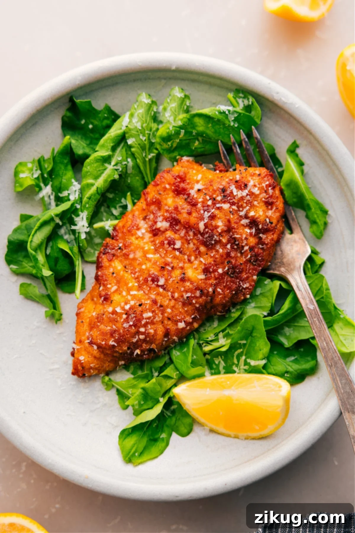 Crispy and delicious Pan-Fried Chicken Cutlets rest on a bed of fresh greens with a bright lemon wedge on the side, ready to be served.