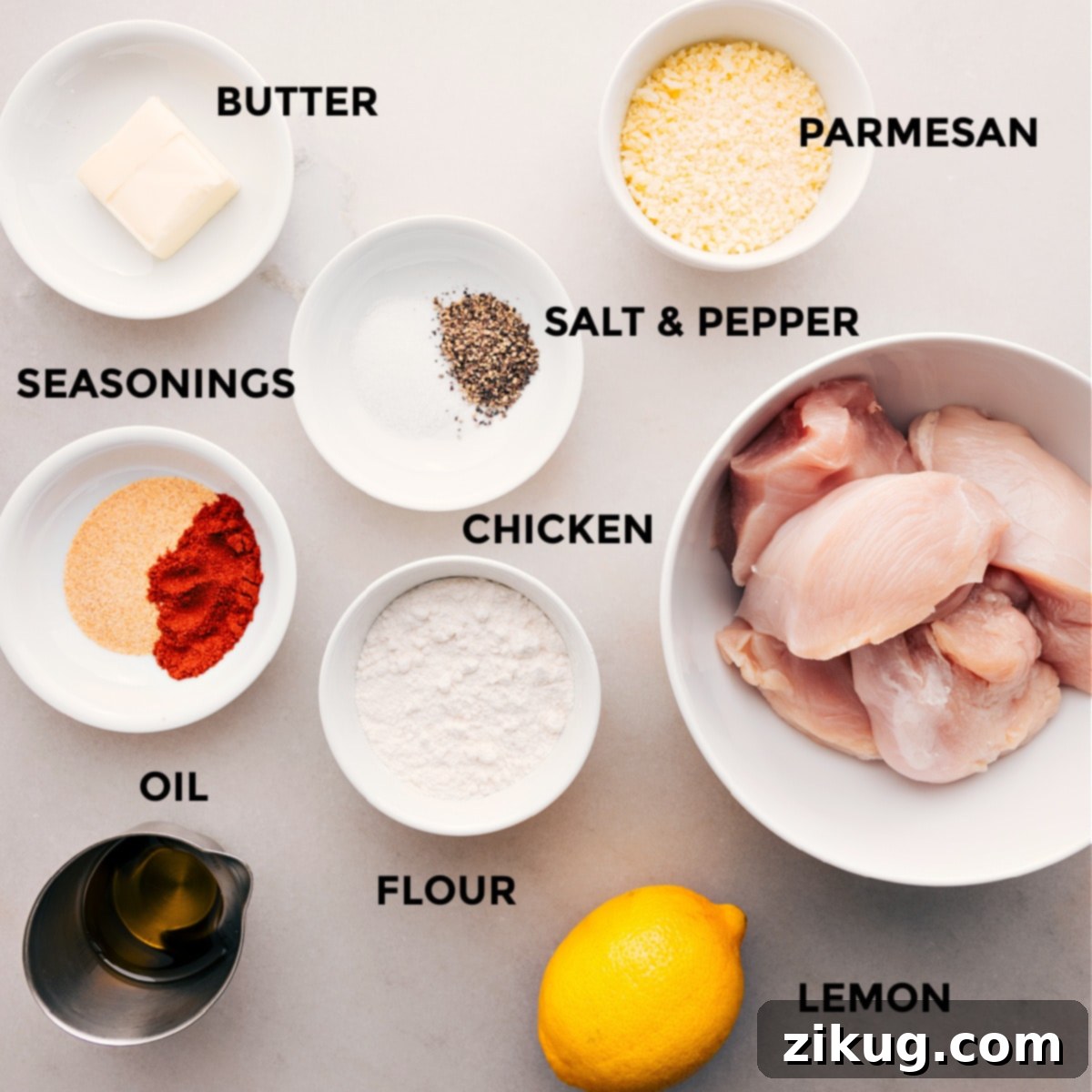 All the fresh ingredients for homemade Chicken Cutlets, including finely grated Parmesan, various seasonings, raw chicken breasts, flour, olive oil, and butter, are neatly prepped and ready for assembly on a countertop.