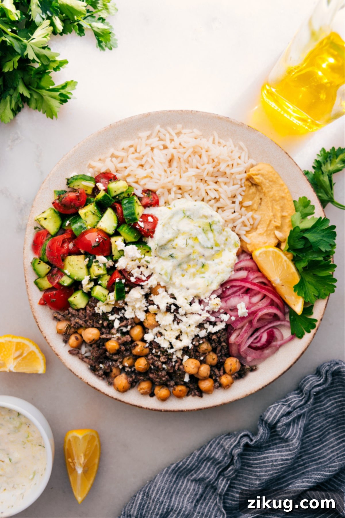 The Best Greek Beef Bowls- Perfect For Meal Prep A beautifully arranged Greek Beef Bowl featuring seasoned ground beef, fluffy white rice, creamy tzatziki, a refreshing Greek salad, tangy pickled red onions, and a rich hummus base.