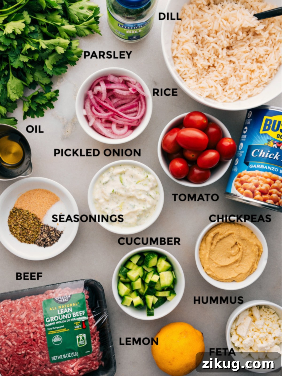 Ingredients In Greek Beef Bowl Recipe All essential ingredients for Greek Beef Bowls are neatly prepped for effortless assembly: freshly sliced red onions, wholesome chickpeas, cooked rice, crisp vegetables, a selection of Greek seasonings, creamy hummus, fresh parsley, crumbled feta cheese, and juicy lemon wedges, alongside the perfectly cooked ground beef.
