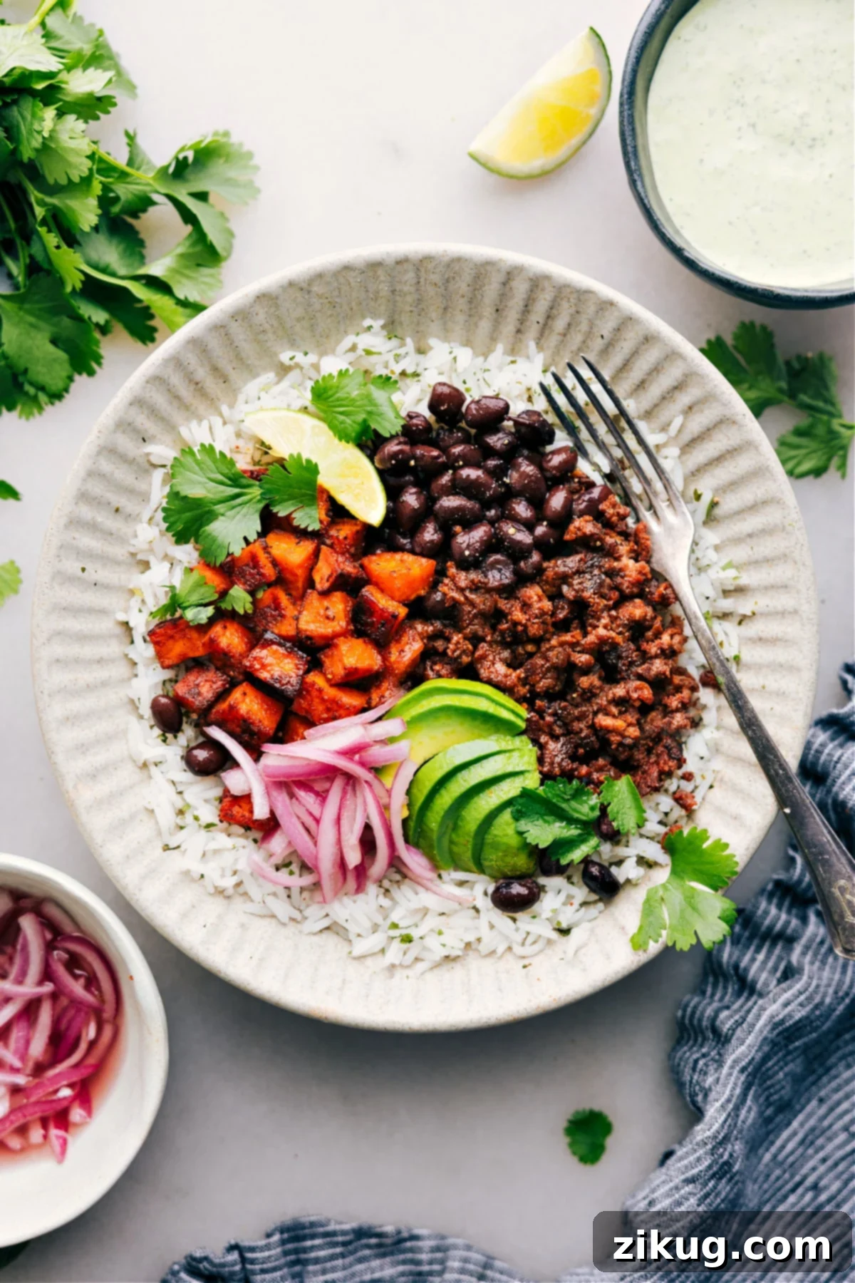 A vibrant Beef Burrito Bowl with fluffy rice, creamy avocado, sharp red onions, and fresh cilantro, drizzled with a rich sauce.